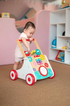 A cute baby is focused on playing with a colorful wooden walker