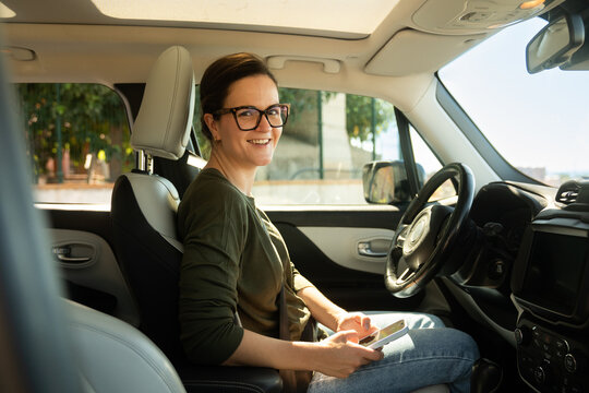 Woman sitting in car checking phone on a sunny day
