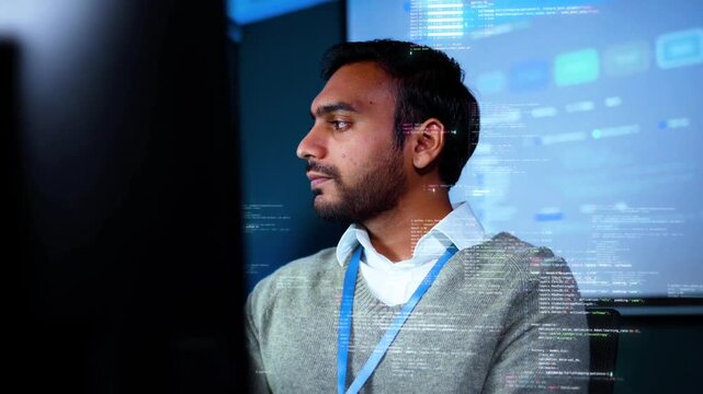 Indian professional software developer writing code working at computer monitor in office with data analytics screens background