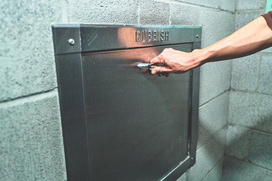 Hand Opening a Metal Rubbish Chute Door on a Concrete Wall