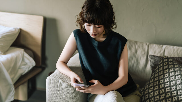 リビングのソファに座ってスマートフォンを使う女性