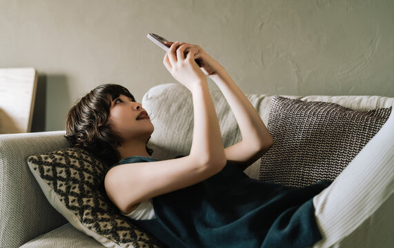 ソファに寝転んでスマートフォンを使う女性