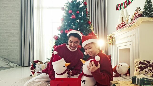 Mother and daughter open Christmas gifts beside a decorated tree