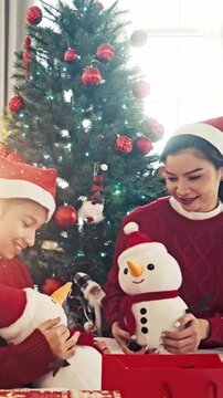 Mother and child share snowman plush toys beside a Christmas tree