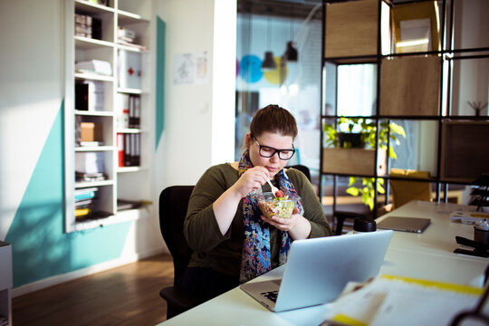 Woman eating salad at desk in office