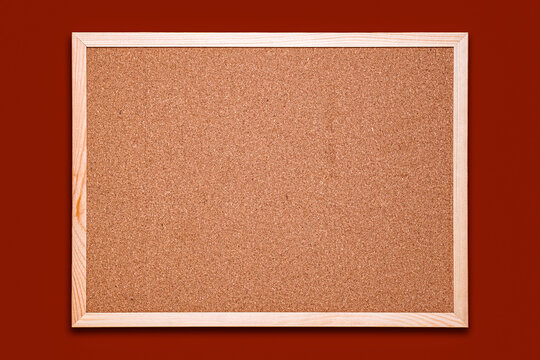 Blank cork bulletin board with wooden frame on solid red wall background.   