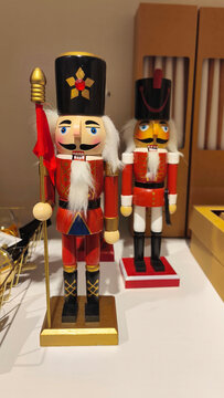 Two traditional wooden nutcracker soldiers in red uniforms, black hats, and gold details displayed indoors as festive Christmas decorations.