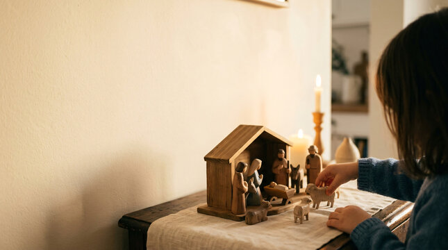 Child playing with wooden nativity scene on a table at home. Traditional Christmas decoration and storytelling.