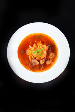 Red broth soup with mushrooms, cabbage, fresh dill in white bowl. Dark background. Healthy homemade meal. Top view