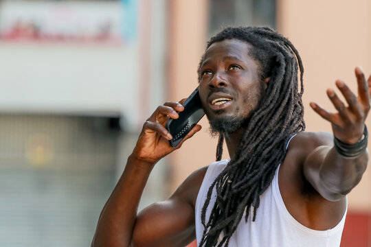 young man with afro hair or dreadlocks talking on mobile phone on the street
