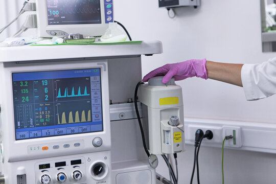 Medical worker in pink glove turns knob on anesthesia machine. Clinical equipment. Monitor shows graphs, tubes, sockets 