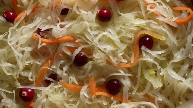 Sauerkraut with carrots and cranberries texture background, rotates. Detailed close up background of traditional fermented sauerkraut mixed with shredded carrots and red cranberries