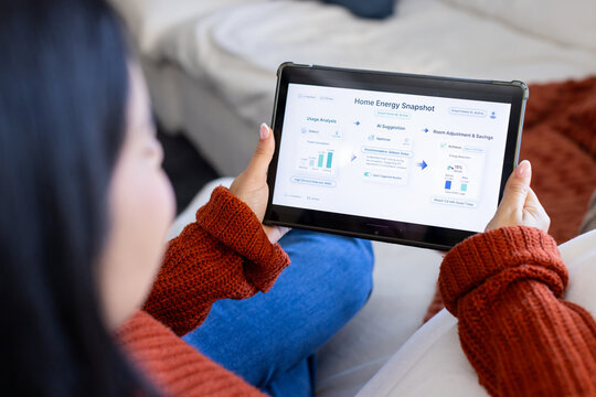 Woman in rust knit sweater holding tablet with energy dashboard while sitting on light sofa