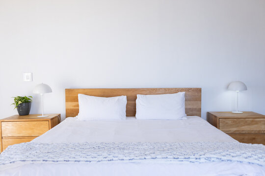 Made bed holding white linens and blue-gray throw beside wooden nightstands with lamps, copy space