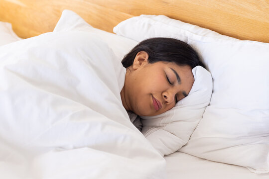Indian woman sleeping on bed with head resting on white pillow under thick duvet