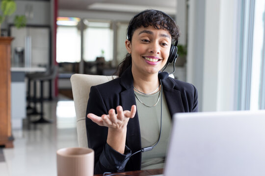 African American woman wearing headset gesturing while speaking at desk with laptop and mug