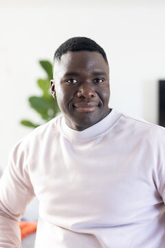 African American man in light pink sweatshirt facing camera against plain wall near blurred plant