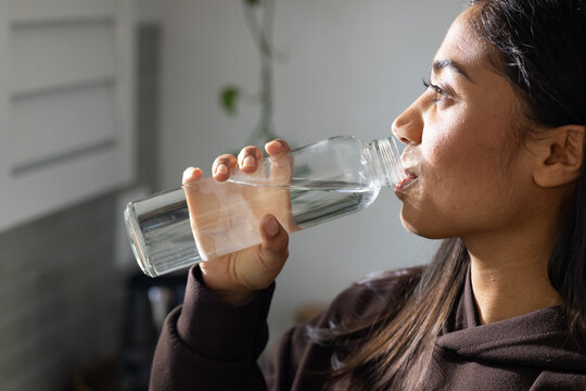 African American woman in profile drinking water from clear plastic bottle in home kitchen