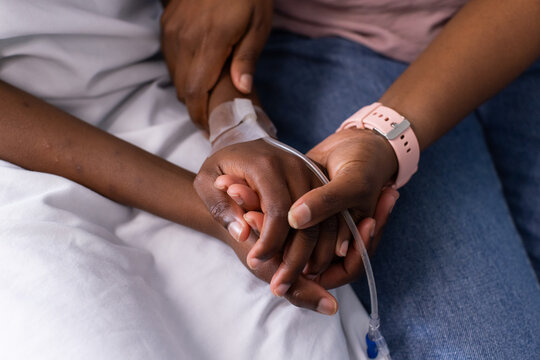 African American caregiver holding child hand with medical tape securing IV line