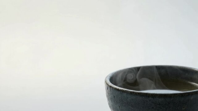 Natural daylight shot of static Japanese ceramic bowl with subtle rising steam, minimalist pale copy space for wellness, mindfulness, and hospitality.