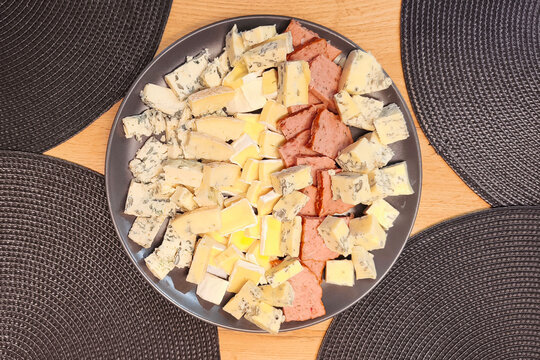 Assorted cheese and sliced meat arranged on a dark plate on a wooden table, ideal for food photography, appetizer presentation, gourmet dining, and entertaining.