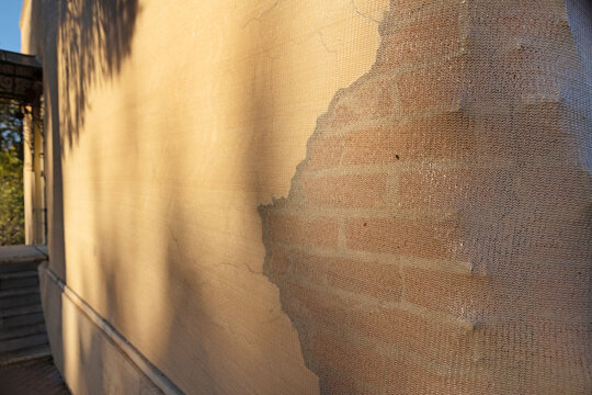 Preservation of historic masonry before restoration. Wall with reinforcing mesh and cracked plaster. Renovation. Sunlight shadow