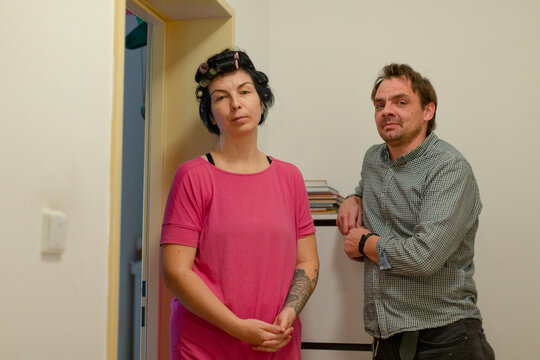Woman with hair rollers and tattoo standing beside man in hallway