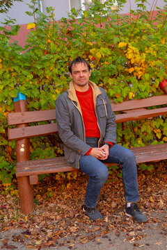 Man sitting on wooden bench in front of leafy shrub during autumn