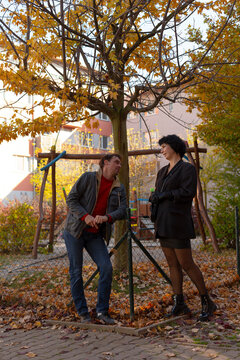 Man and woman talking by fenced tree in autumn courtyard (daylight)