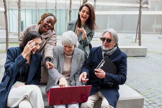 diverse business group of people sitting together using laptop outdoors at cityscape. Successful Entrepreneurs multiracial and multigenerational teamwork in city morning in winter