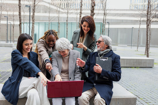 diverse business group of people sitting together using laptop outdoors at cityscape. Successful Entrepreneurs multiracial and multigenerational teamwork in city morning in winter