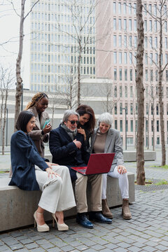 diverse business group of people sitting together using laptop outdoors at cityscape. Successful Entrepreneurs multiracial and multigenerational teamwork in city morning in winter