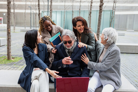 diverse business group of people sitting together using laptop outdoors at cityscape. Successful Entrepreneurs multiracial and multigenerational teamwork in city morning in winter