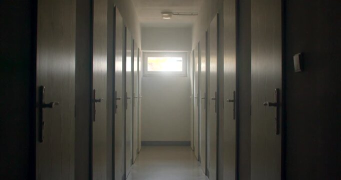 Narrow school corridor with rows of closed doors and distant window of