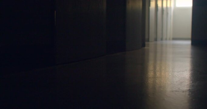 Low-angle school corridor with reflective floor and distant daylight