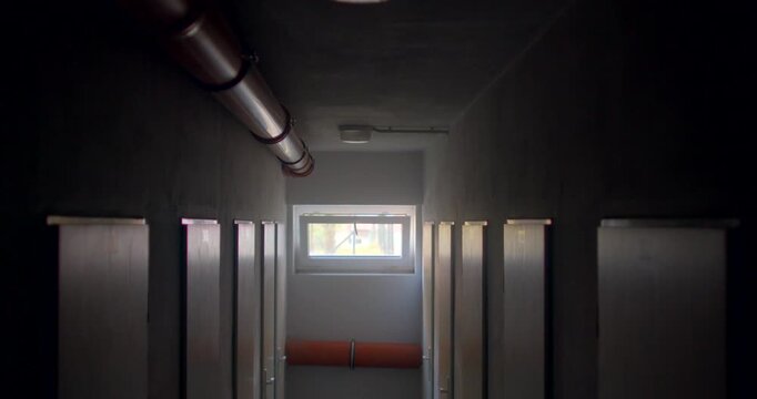 Narrow school corridor with lockers and small window at far end in dim