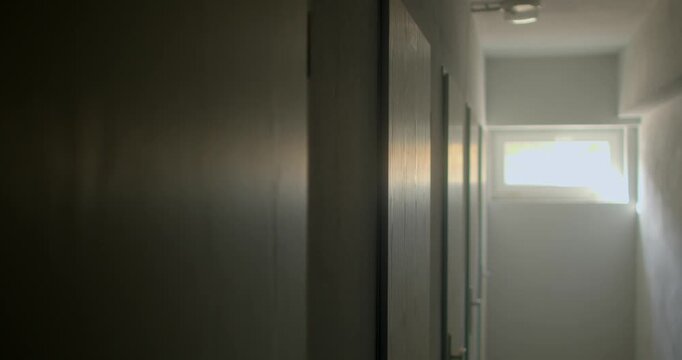 Dim school corridor with row of closed wooden doors and bright window