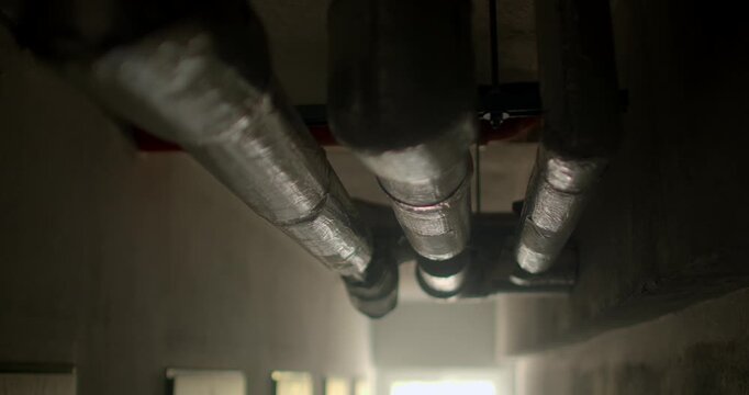 Insulated metal pipes running along corridor ceiling in dim utility or