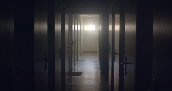 Dim narrow corridor lined with wooden doors leading to bright window