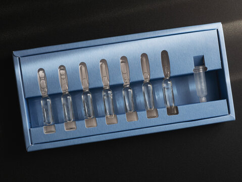 Glass Skincare Serum Ampoules in Blue Packaging on Dark Background