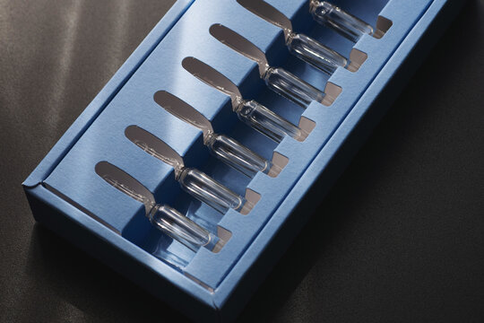 Glass Skincare Serum Ampoules in Blue Packaging on Dark Background