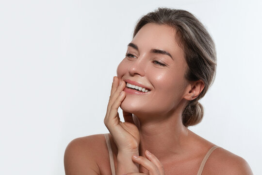Beauty portrait of a smiling woman with radiant skin, subtle makeup posing against a white background