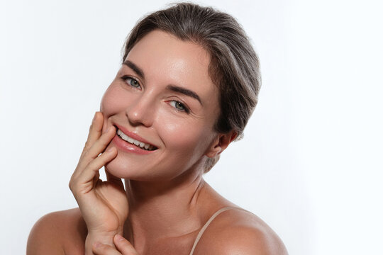 Beauty portrait of a smiling woman with radiant skin, subtle makeup posing against a white background