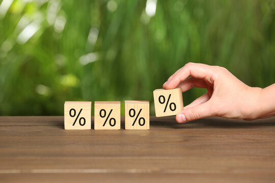 Man placing cube with percent sign next to others on wooden table, closeup. Discount concept