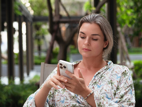 Woman Using Smartphone While Sitting at Outdoor Terrace Surrounded by Greenery