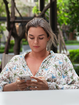 Woman Using Smartphone While Sitting at Outdoor Terrace Surrounded by Greenery