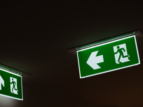 Illuminated Green Emergency Exit Direction Sign with White Right Arrow Hanging in Dark Indoor Corridor, Safety and Evacuation Concept