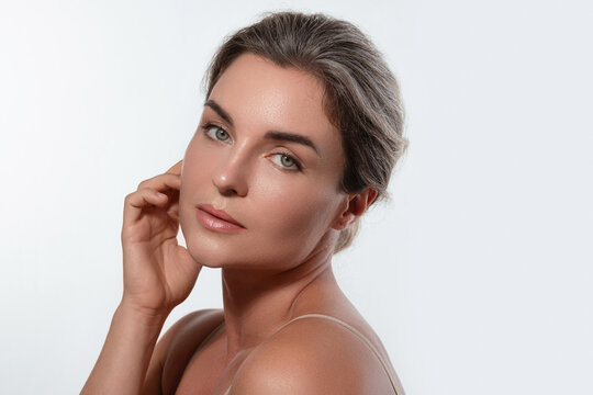 Beauty portrait of a woman with radiant skin, subtle makeup posing against a white background.