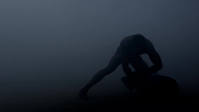 MMA fighter punching heavy bag floor fog. Ground and pound training dark studio.