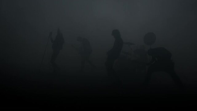 Drummer bassist guitarist performing mist. Rock musicians silhouette handheld.